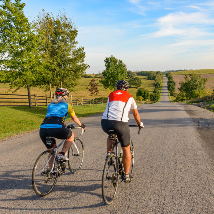 2 people on bikes riding away from camera on a country road