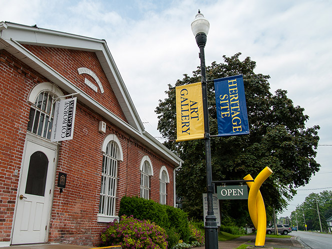 Exterior view of Colborne Art Gallery with yellow sculpture and flag signs in front