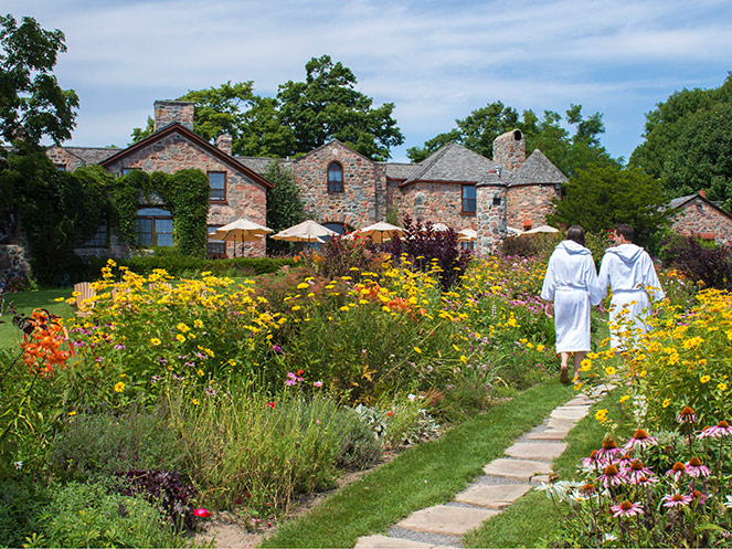 Couple walking up flower-lined walkway towards stone building at Ste. Anne's Spa